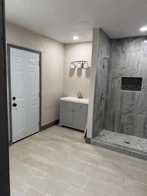 bathroom featuring a textured ceiling, vanity, and tiled shower