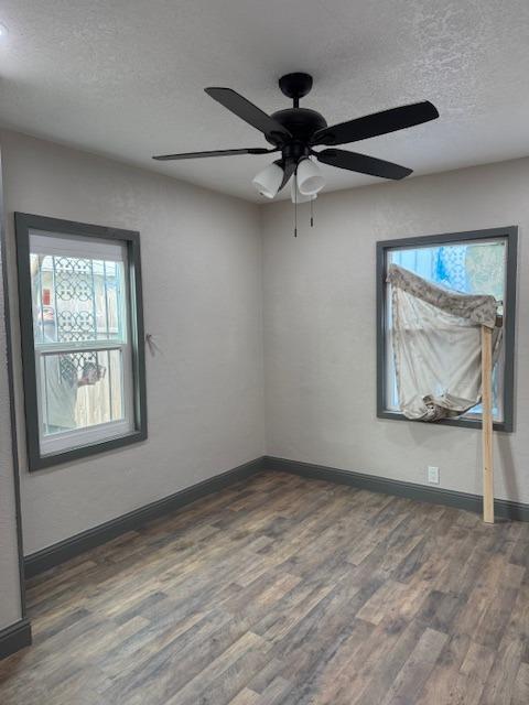 empty room with a textured ceiling, ceiling fan, a healthy amount of sunlight, and dark hardwood / wood-style floors