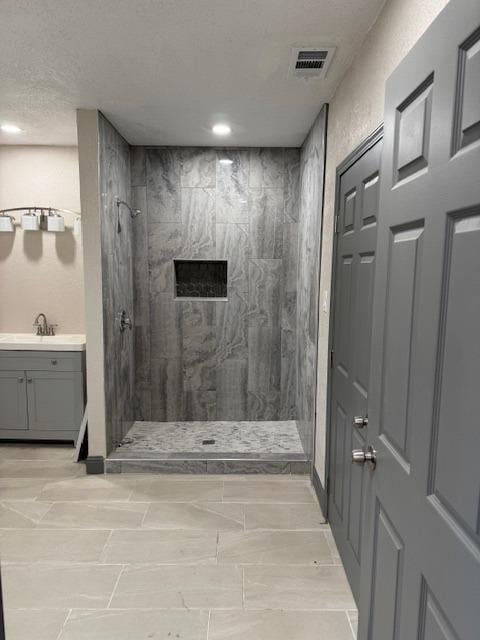 bathroom featuring a tile shower, vanity, and a textured ceiling