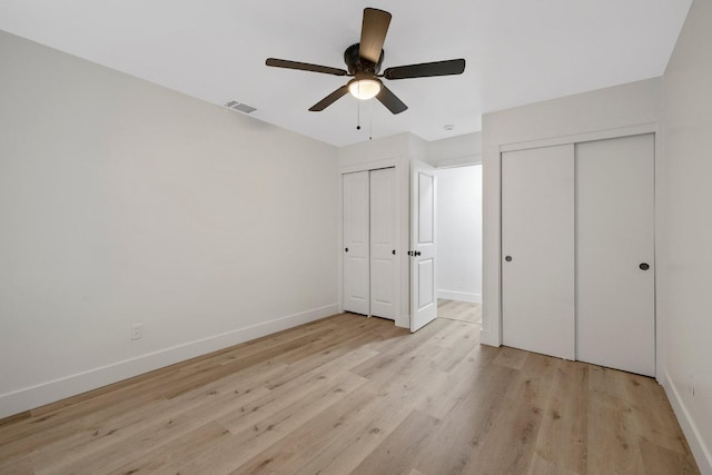 unfurnished bedroom featuring ceiling fan, light hardwood / wood-style floors, and multiple closets