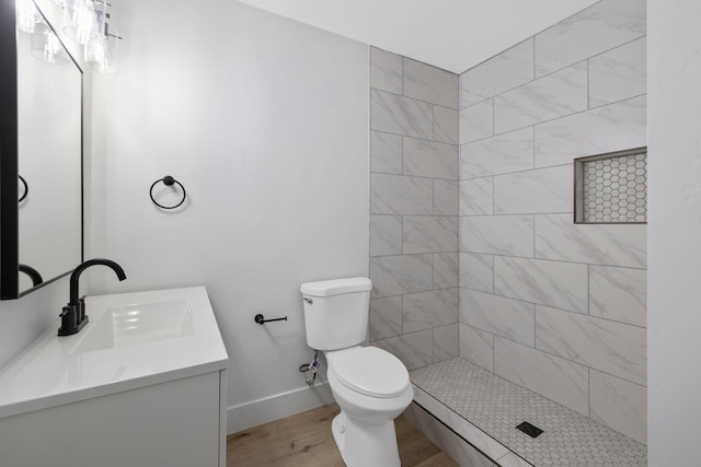 bathroom featuring hardwood / wood-style floors, vanity, a tile shower, and toilet