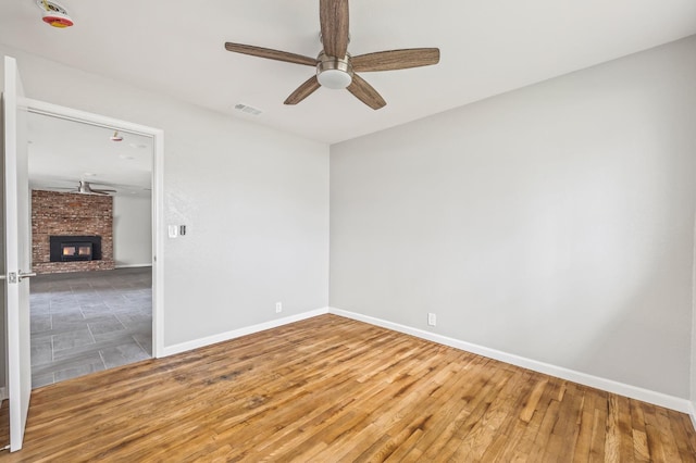 empty room with a brick fireplace, wood-type flooring, and ceiling fan