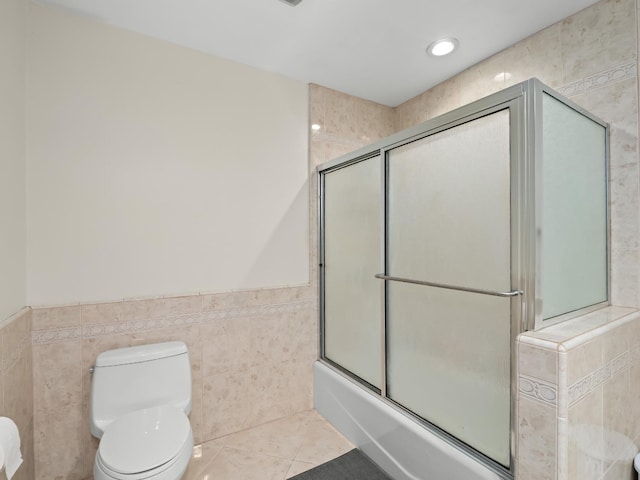 bathroom featuring tile patterned floors, enclosed tub / shower combo, tile walls, and toilet