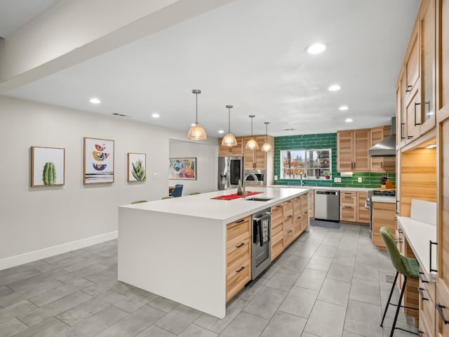 kitchen featuring stainless steel appliances, wall chimney range hood, tasteful backsplash, an island with sink, and pendant lighting