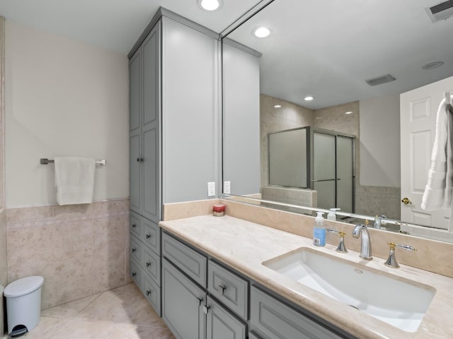 bathroom with tile patterned floors, vanity, a shower with shower door, and tile walls