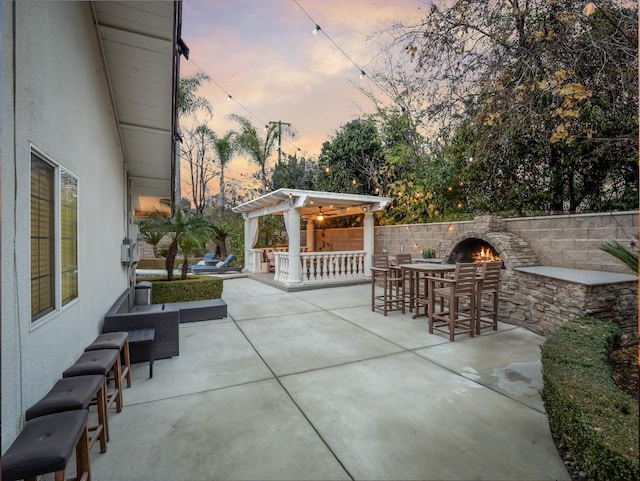 patio terrace at dusk with an outdoor stone fireplace and exterior bar