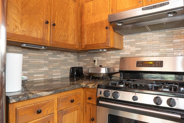 42135 Hanging Branch Rd, Shaver Lake, CA 93664 - kitchen with stainless steel gas stove, under cabinet range hood, decorative backsplash, brown cabinetry, and dark stone countertops
