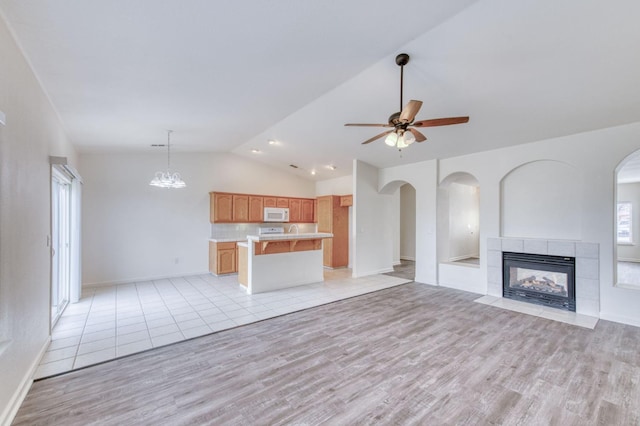 unfurnished living room with a tile fireplace, ceiling fan with notable chandelier, light hardwood / wood-style floors, and lofted ceiling