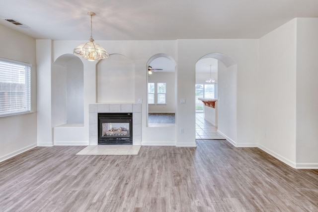 unfurnished living room with ceiling fan with notable chandelier, light hardwood / wood-style floors, and a tiled fireplace