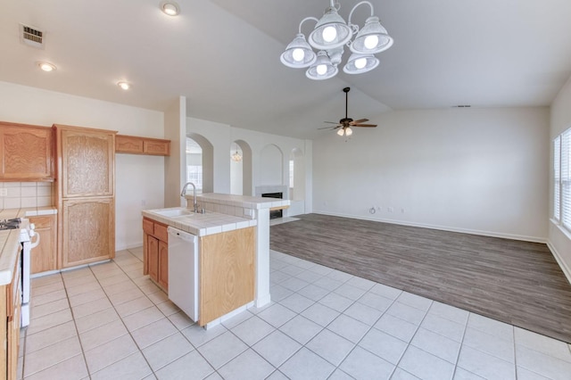 kitchen featuring white appliances, vaulted ceiling, tile countertops, light hardwood / wood-style flooring, and an island with sink