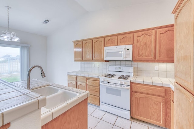 kitchen featuring tile countertops, a chandelier, white appliances, and vaulted ceiling