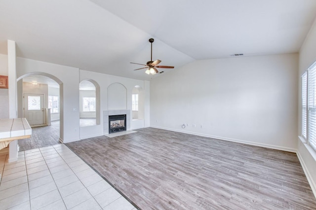 unfurnished living room featuring a tiled fireplace, ceiling fan, plenty of natural light, and light hardwood / wood-style floors