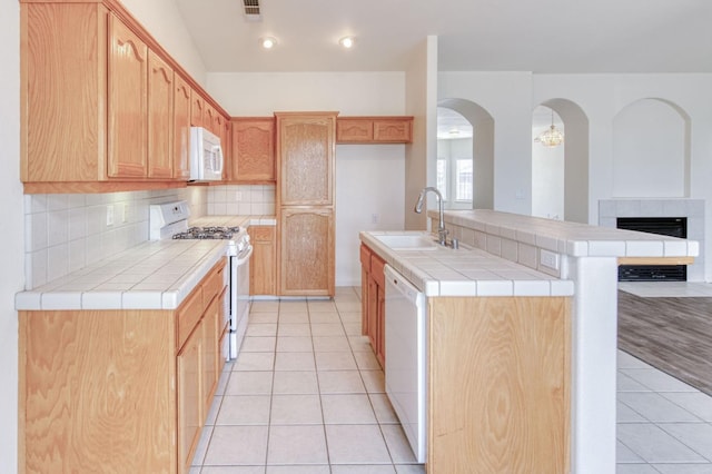 kitchen with tile counters, sink, white appliances, a tiled fireplace, and a center island with sink