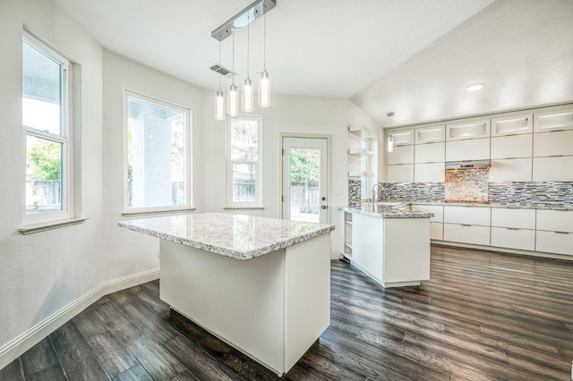 kitchen with a healthy amount of sunlight, white cabinetry, hanging light fixtures, dark wood-type flooring, and a center island with sink