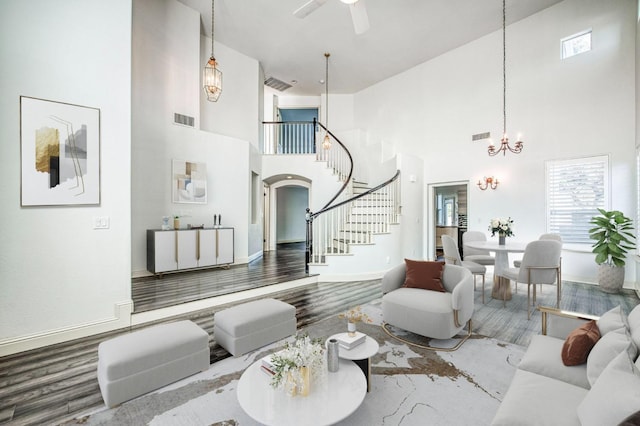 living room featuring a towering ceiling, ceiling fan with notable chandelier, and wood-type flooring