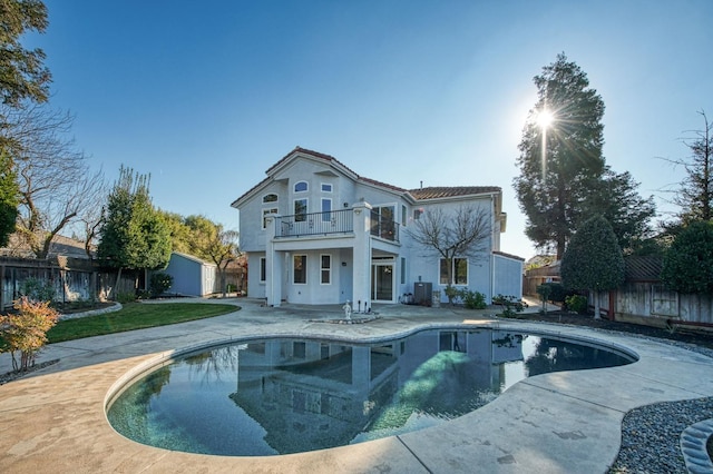 rear view of house with a fenced in pool, a patio area, and a balcony