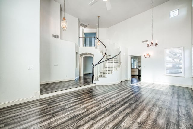 unfurnished living room with wood-type flooring, a towering ceiling, and ceiling fan with notable chandelier