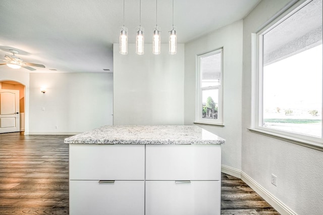 kitchen featuring pendant lighting, ceiling fan, light stone counters, white cabinets, and dark hardwood / wood-style flooring