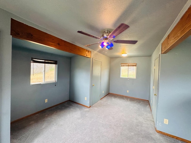 unfurnished bedroom with a textured ceiling, light colored carpet, multiple windows, and ceiling fan