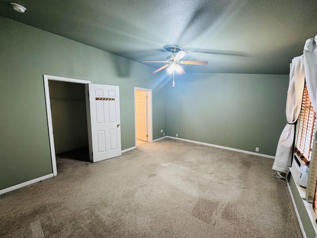 unfurnished bedroom with lofted ceiling, a walk in closet, ceiling fan, a textured ceiling, and carpet floors