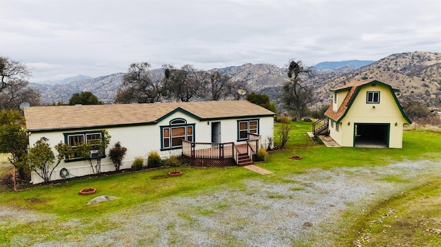 view of front of house with a deck with mountain view, an outdoor fire pit, a front yard, a garage, and an outbuilding