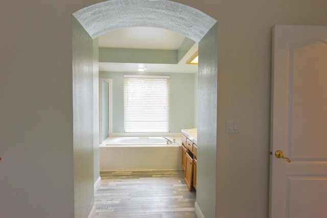 bathroom with hardwood / wood-style floors, vanity, and tiled tub