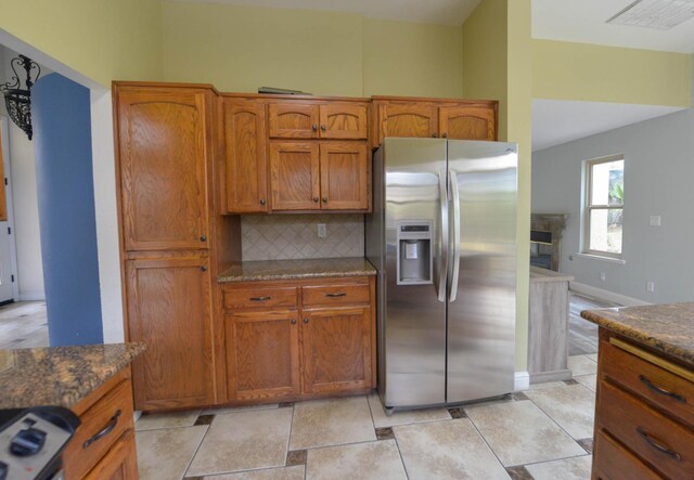 kitchen featuring backsplash, dark stone counters, range, light tile patterned floors, and stainless steel fridge with ice dispenser