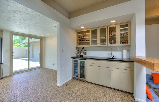 bar with wine cooler, sink, white cabinets, and a textured ceiling