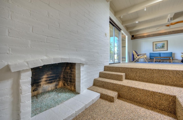 stairway with beam ceiling, brick wall, and a brick fireplace