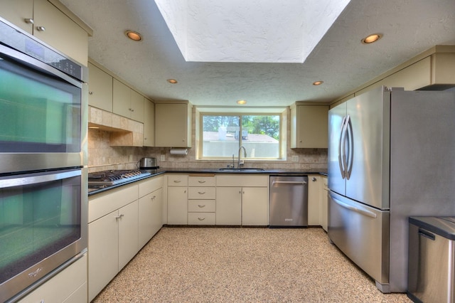 kitchen featuring decorative backsplash, a textured ceiling, stainless steel appliances, sink, and cream cabinets