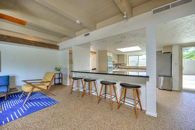 kitchen featuring kitchen peninsula, a breakfast bar, stainless steel appliances, sink, and beamed ceiling