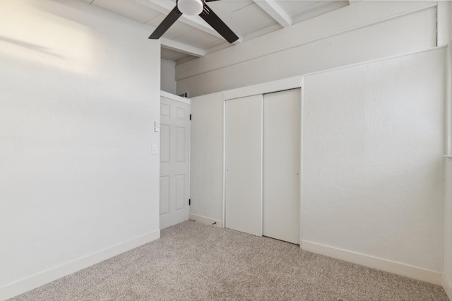 unfurnished bedroom featuring beam ceiling, a closet, ceiling fan, and carpet