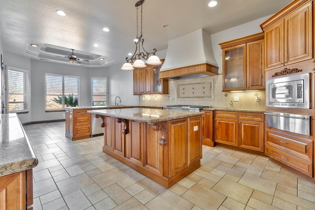 kitchen featuring ceiling fan with notable chandelier, stainless steel appliances, a kitchen island, and custom exhaust hood