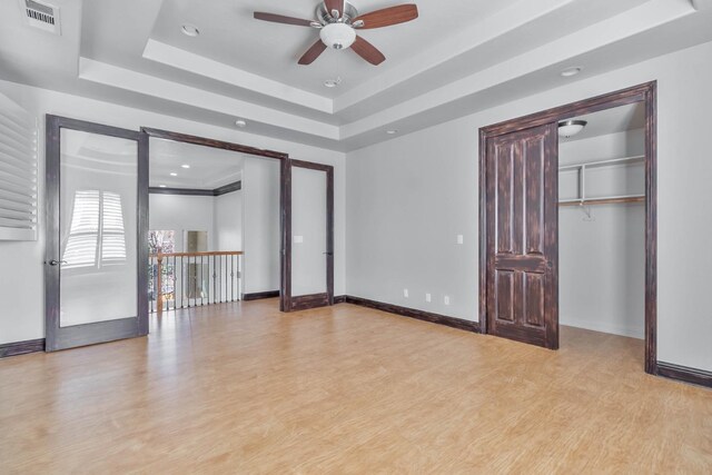 unfurnished bedroom with ceiling fan, light hardwood / wood-style floors, and a tray ceiling