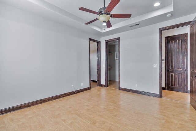 unfurnished bedroom with a walk in closet, light hardwood / wood-style floors, a raised ceiling, and ceiling fan