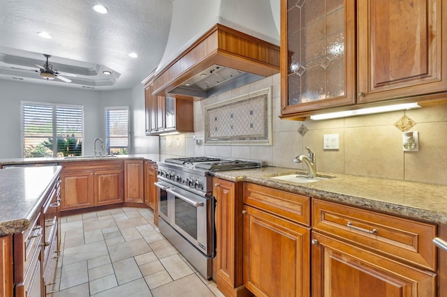 kitchen with custom exhaust hood, high end range, backsplash, a raised ceiling, and sink