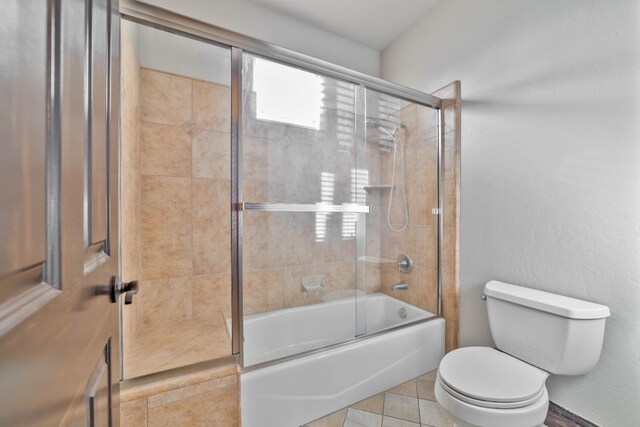 bathroom with tile patterned flooring, toilet, and combined bath / shower with glass door