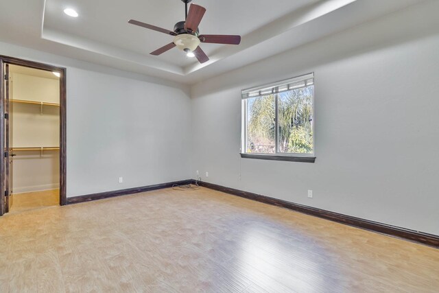 unfurnished bedroom featuring light wood-type flooring, a walk in closet, a tray ceiling, and ceiling fan