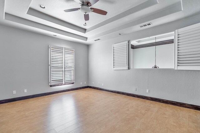 empty room with a tray ceiling, ceiling fan, and light hardwood / wood-style flooring