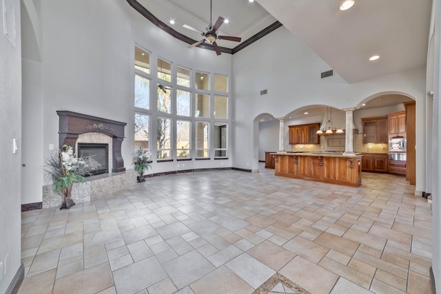 living room with ornate columns, crown molding, ceiling fan, and a high ceiling