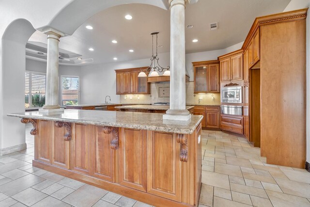 kitchen with kitchen peninsula, tasteful backsplash, light stone counters, decorative columns, and stainless steel microwave