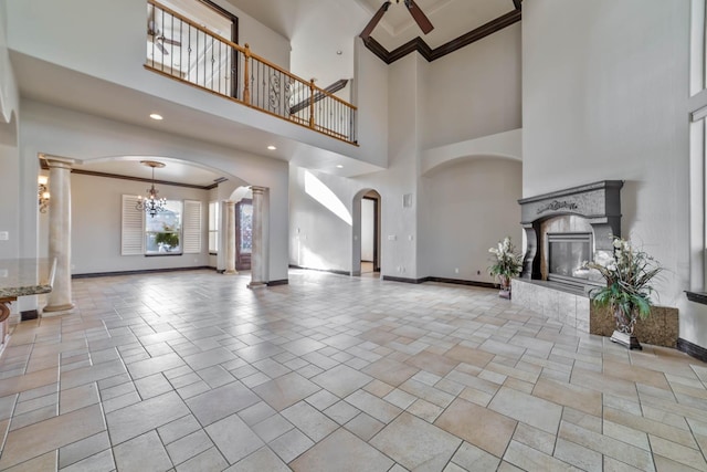 unfurnished living room with ceiling fan with notable chandelier, a towering ceiling, and crown molding