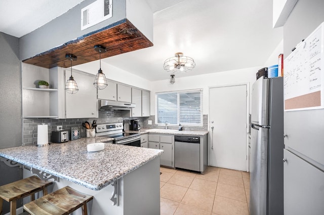 kitchen featuring kitchen peninsula, decorative light fixtures, a kitchen bar, gray cabinets, and appliances with stainless steel finishes