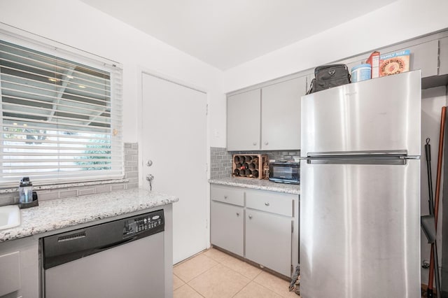 kitchen featuring decorative backsplash, light stone counters, light tile patterned floors, and stainless steel appliances