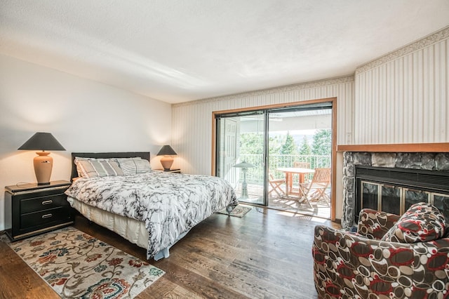 bedroom with access to exterior, a textured ceiling, a stone fireplace, and dark wood-type flooring