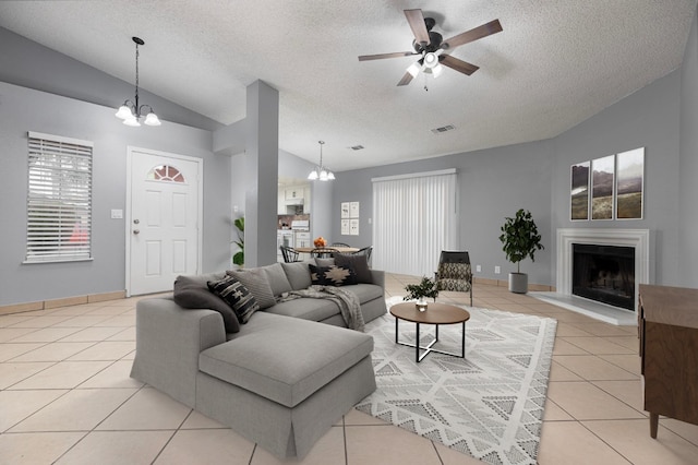 living room with ceiling fan with notable chandelier, light tile patterned floors, a textured ceiling, and vaulted ceiling