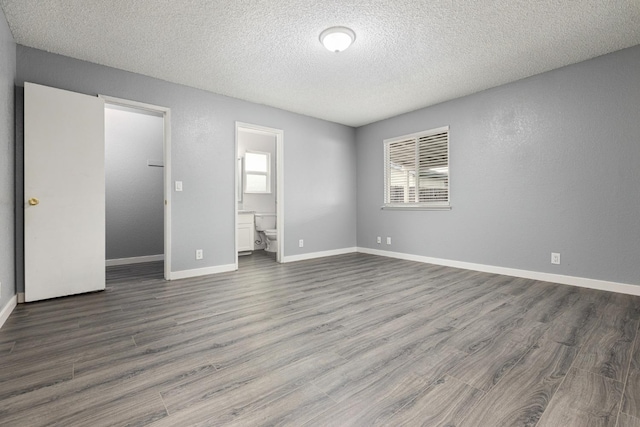 unfurnished bedroom with a textured ceiling, a spacious closet, dark wood-type flooring, and ensuite bath