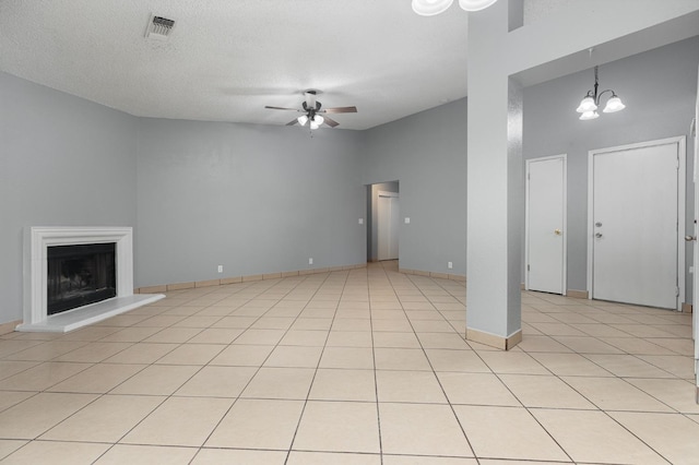 unfurnished living room with ceiling fan with notable chandelier, light tile patterned floors, a textured ceiling, and a towering ceiling