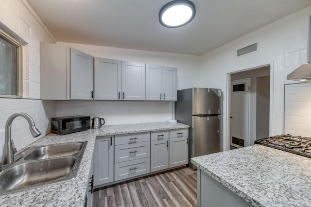 kitchen featuring gray cabinetry, backsplash, sink, wood-type flooring, and stainless steel refrigerator