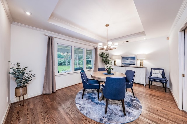 dining area featuring a raised ceiling, crown molding, wood-type flooring, and a notable chandelier